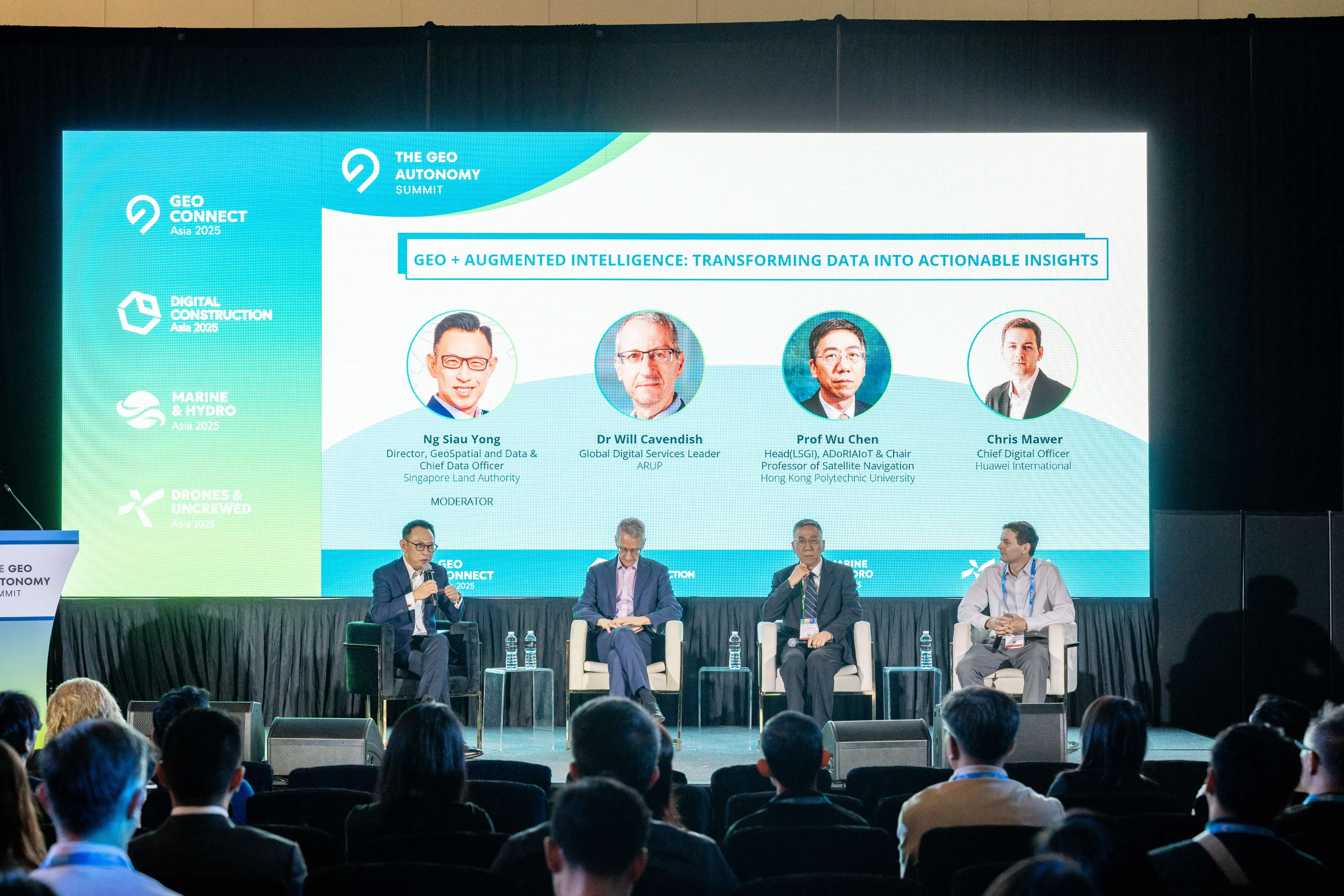 Four panelists seated on stage before an audience, with a large screen to talk about Geo Augmented Intelligence: Transforming Data Into Actionable Insights..